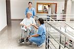 Two nurses looking after old women sitting in wheelchair and holding her hand