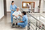 Two nurses talking with old women sitting in wheelchair and smiling