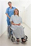 Happy nurse and patient in wheelchair in hospital corridor