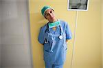 Thoughtful nurse in scrubs leaning against wall in hospital room