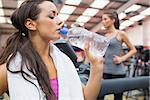 Woman drinking bottle of water in the gym during exercise