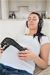 Pregnant woman listening to music and holding headphones on belly in living room