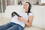 Pregnant woman holding headphones to belly and listening to music in lving room
