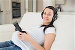 Prospective mother lying on the couch listening to music and holding headphones to belly