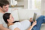 Young prospective parents lying on the couch while using the ebook