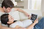 Prospective parents looking at ultrasound scan on tablet pc on sofa in living room