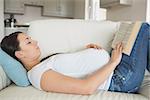 Young pregnant woman with her hand on her belly reading a book on sofa