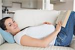 Pregnant woman with a hand on her belly lying on the couch while reading a book