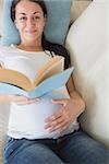 Young pregnant woman reading a book while relaxing on the couch