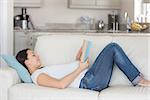 Pregnant woman relaxing and reading book on sofa