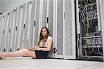 Happy woman sitting on floor working on laptop in data center