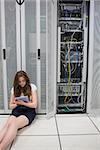 Woman working on servers with tablet pc sitting on floor in data center