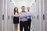 Three smiling technicians standing in data center with arms crossed