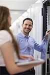 Technician smiling at colleague holding laptop in data center