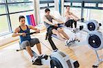 Three people on rowing machines in fitness studio