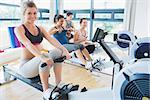 Smiling woman on rowing machine with others in fitness studio