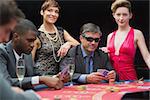 Man in sunglasses playing poker with two women either side in casino