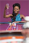 Woman sitting at a roulette table raising her glass