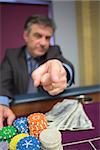 Man with chips and cash pointing sitting at roulette table