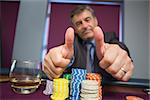 Man giving thumbs up sitting at roulette table in casino