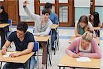 Student raising hand during exam in exam hall in college