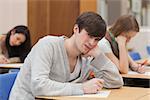 Boy looking up from exam and frowning in college classroom
