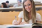 Woman sitting at the lecture hall while writing and smiling