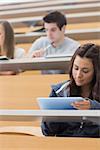 Woman sitting at the lecture hall holding a tablet computer and using it to take notes