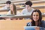 Smiling student taking notes with tablet pc in lecture hall