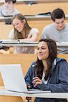 Girl sitting in lecture hall using laptop and smiling