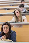 Student sitting reading a book while smiling in lecture hall