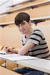 Man sitting at the lecture hall while smiling and making notes