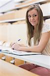 Girl sitting at the lecture hall writing notes and smiling