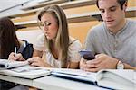 Student using smartphone in lecture hall with other student studying