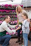 Employee giving a flower to little girl while her mother standing next to her in garden center