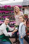 Employee giving flower pot to little girl with mother in garden center