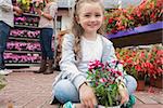 Little girl holding flowers while smiling sitting on path of garden center