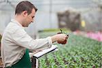 Man standing in greenhouse nursery and taking notes