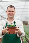Cheerful gardener holding a plant in greenhouse