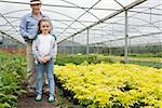 Little girl with grandfather standing and smiling in greenhouse