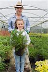 Little girl holding potted plant with grandfather in the greenhouse
