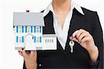 Businesswoman in suit holding a model house and key against white background