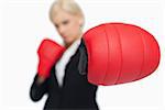 Blonde businesswoman with red boxing gloves fighting against white background
