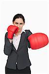 Serious brunette wearing red gloves while punching against white background