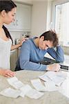 Wife comforting stressed husband over bills in kitchen with tablet pc