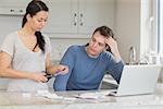 Wife cutting up credit card with husband watching in kitchen with laptop