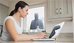 Young woman seeing reflection of robber in laptop screen