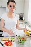Young woman tossing salad fro sandwich in kitchen