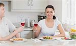 Two young people eating sandwiches and drinking wine in the kitchen