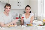Young couple sitting in the kitchen while drinking wine and eating sandwiches